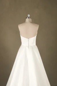Back view of a satin wedding dress on a mannequin, featuring a simple button closure and a full skirt, ideal for bridal shops.