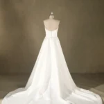 Back view of a strapless white bridal gown on a mannequin, featuring a long flowing train. Ideal for upscale weddings.