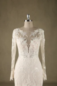 Detailed wedding dress featuring intricate lace and sheer long sleeves displayed on a mannequin against a neutral background.