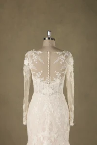 Back view of an elegant ivory wedding dress with floral lace design and button down detail on a mannequin, showcasing craftsmanship.