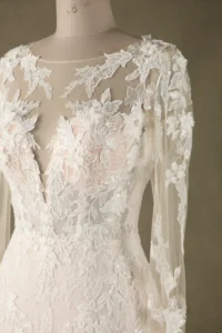 Close-up of a bridal gown showcasing intricate white lace embroidery, delicate floral patterns, and sheer fabric detailing on sleeves and bodice.