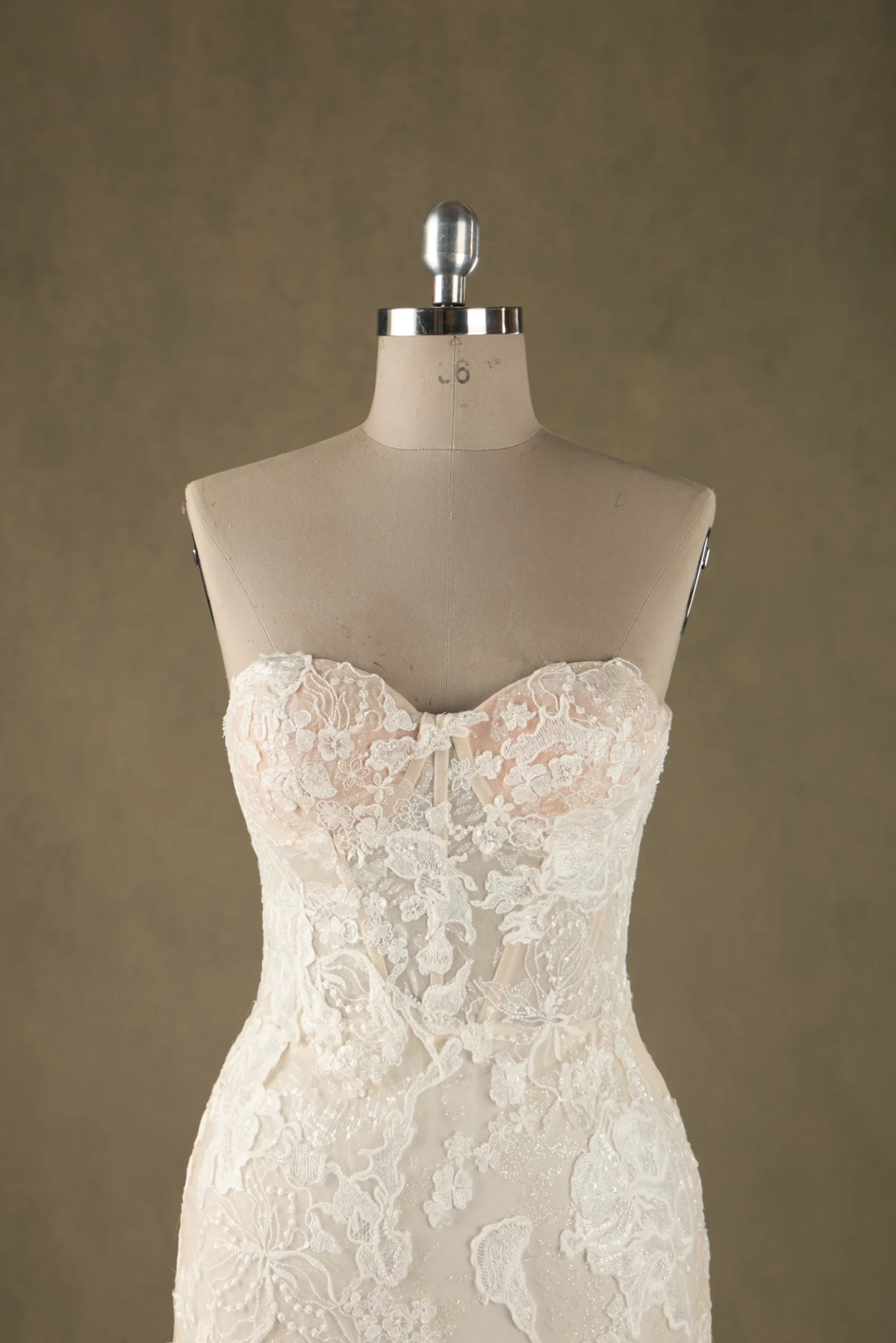 A close-up view of a lace strapless wedding dress on a mannequin, showcasing intricate floral lace details.