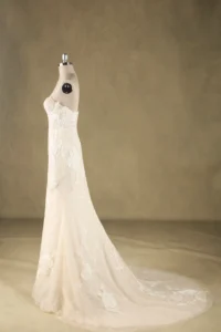 A strapless, lace wedding dress displayed on a mannequin against a neutral background, showcasing intricate floral embroidery and a long train.