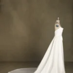 A strapless white wedding dress displayed on a mannequin, featuring a long flowing train against a neutral backdrop.