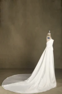 A strapless white wedding dress displayed on a mannequin, featuring a long flowing train against a neutral backdrop.