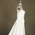 Elegant strapless wedding dress on a mannequin, showcasing pleated bodice and flowing skirt against a neutral background.