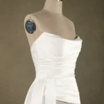 White strapless wedding dress displayed on a mannequin, featuring a fitted bodice and draped front detailing, photographed indoors.