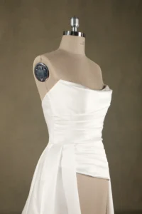 White strapless wedding dress displayed on a mannequin, featuring a fitted bodice and draped front detailing, photographed indoors.