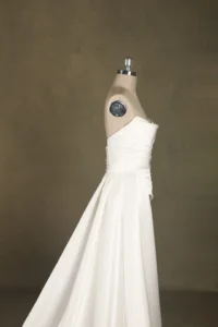 Elegant strapless wedding dress on a mannequin, showcasing pleated bodice and flowing skirt against a neutral background.