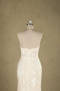 Back view of an elegant wedding dress with intricate lace details displayed on a mannequin against a neutral background.