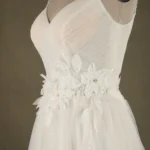 Close-up of a wedding dress featuring a floral applique design with sequins on a mannequin.