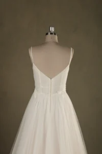 Back view of an elegant backless wedding dress with delicate straps on a mannequin, showcasing intricate detailing and flowing skirt.