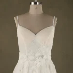 Close-up of an elegant bridal gown on a mannequin, featuring intricate floral detailing and delicate straps, showcased by SisterBridal.