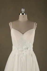 Close-up of an elegant bridal gown on a mannequin, featuring intricate floral detailing and delicate straps, showcased by SisterBridal.