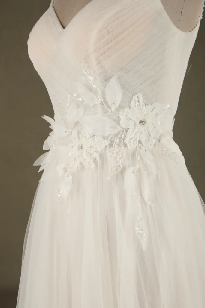 Close-up of an elegant bridal gown featuring delicate floral embellishments and intricate beading on a flowing white fabric.