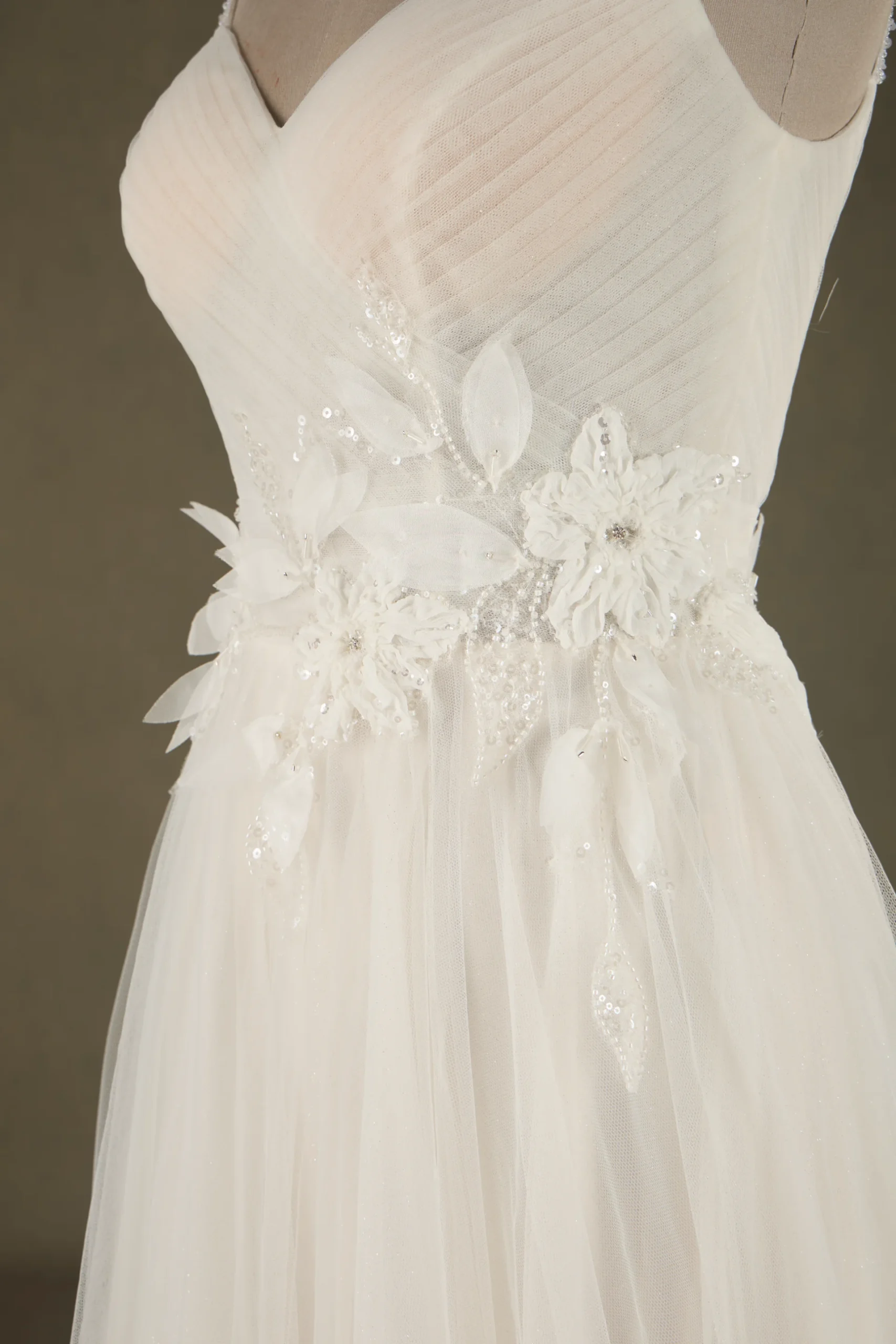 Close-up of an elegant bridal gown featuring delicate floral embellishments and intricate beading on a flowing white fabric.