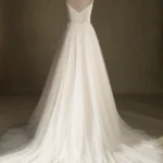 Back view of an elegant tulle wedding dress with thin straps and a flowing train displayed on a mannequin.