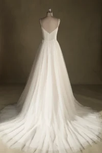 Back view of an elegant tulle wedding dress with thin straps and a flowing train displayed on a mannequin.