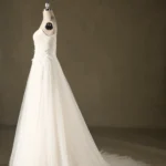 A flowing white wedding dress with a long train displayed on a mannequin against a plain backdrop.