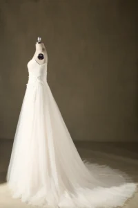 A flowing white wedding dress with a long train displayed on a mannequin against a plain backdrop.