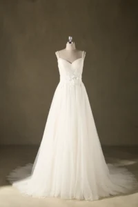 White bridal gown displayed on a mannequin against a neutral background, featuring delicate floral details and flowing tulle skirt.