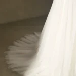Close-up view of an elegant white bridal gown train with soft tulle fabric spread on a neutral background.