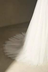 Close-up view of an elegant white bridal gown train with soft tulle fabric spread on a neutral background.