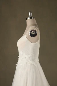 Side view of an elegant white wedding dress on a mannequin, featuring a floral lace design and sleek bodice.